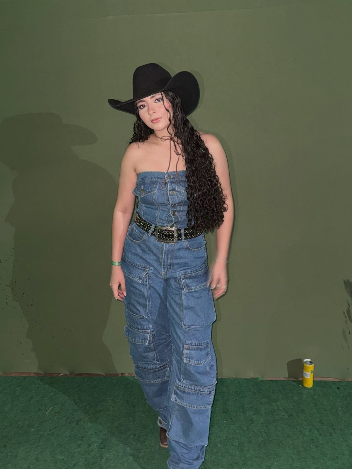 Woman wearing a black cowboy hat and strapless denim cargo jumpsuit posing indoors.