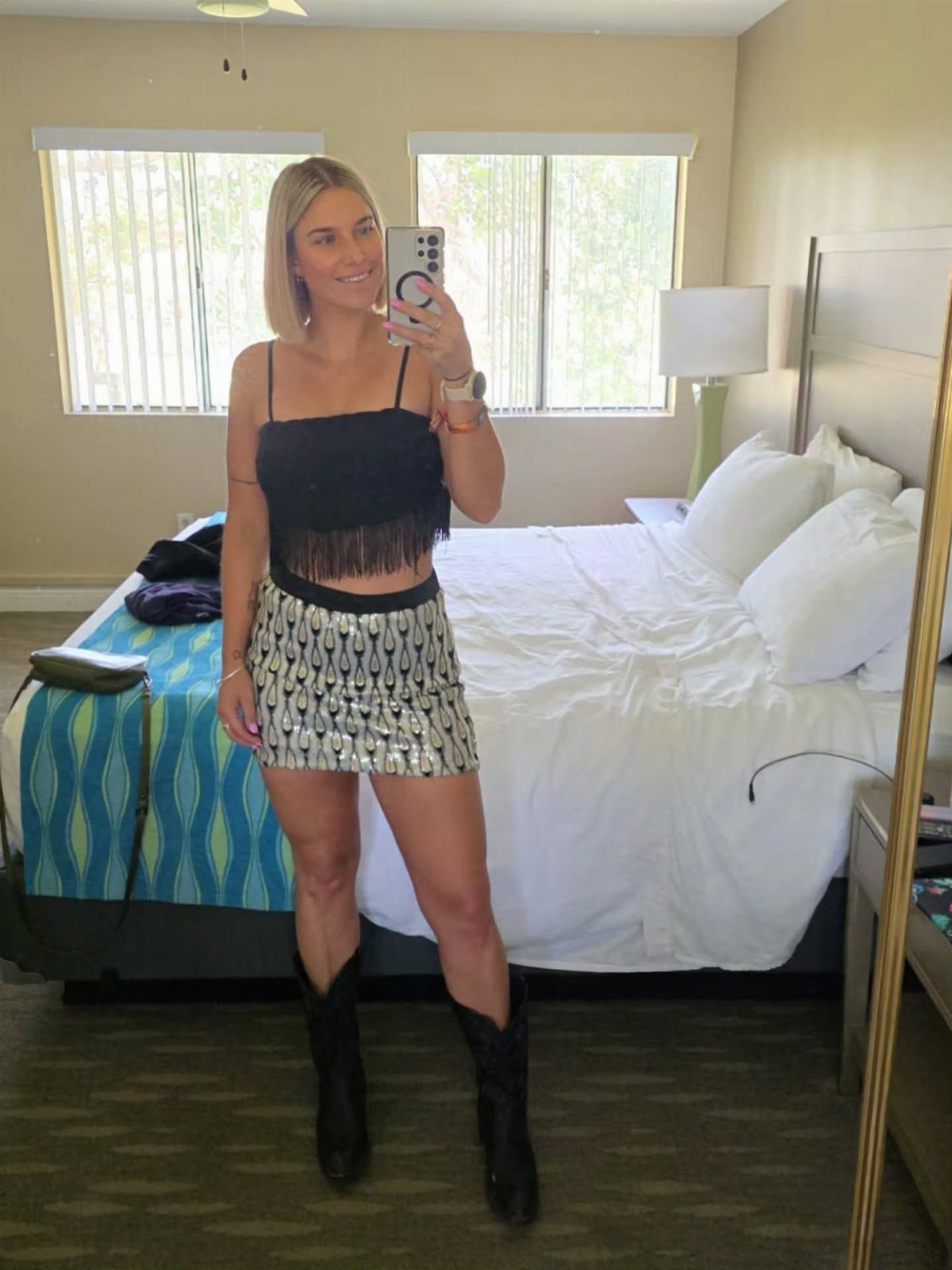 Woman wearing a black fringed top, silver metallic miniskirt, and black cowboy boots.