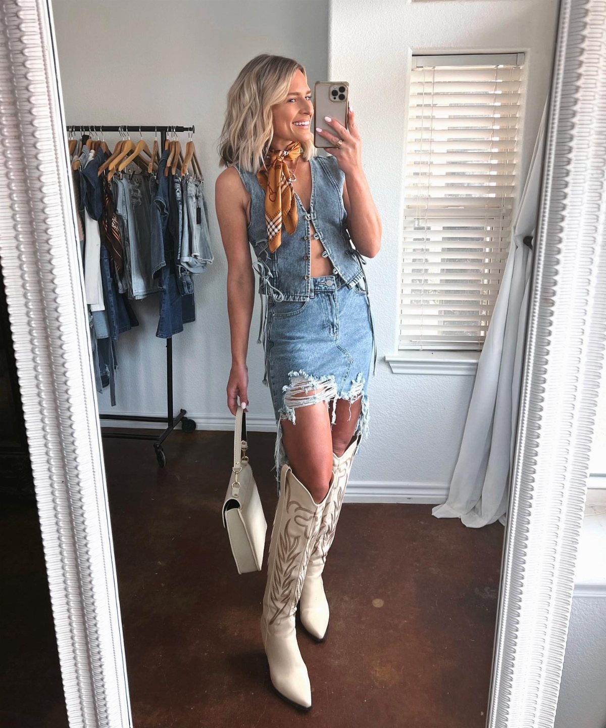 Woman in denim two-piece set and white cowboy boots taking a mirror selfie.