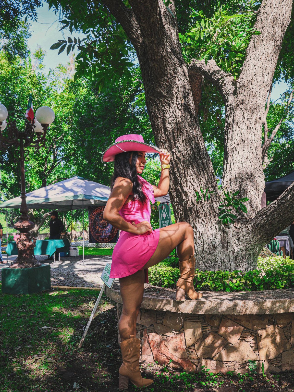Woman in pink mini dress, pink cowboy hat, and brown boots posing outdoors.