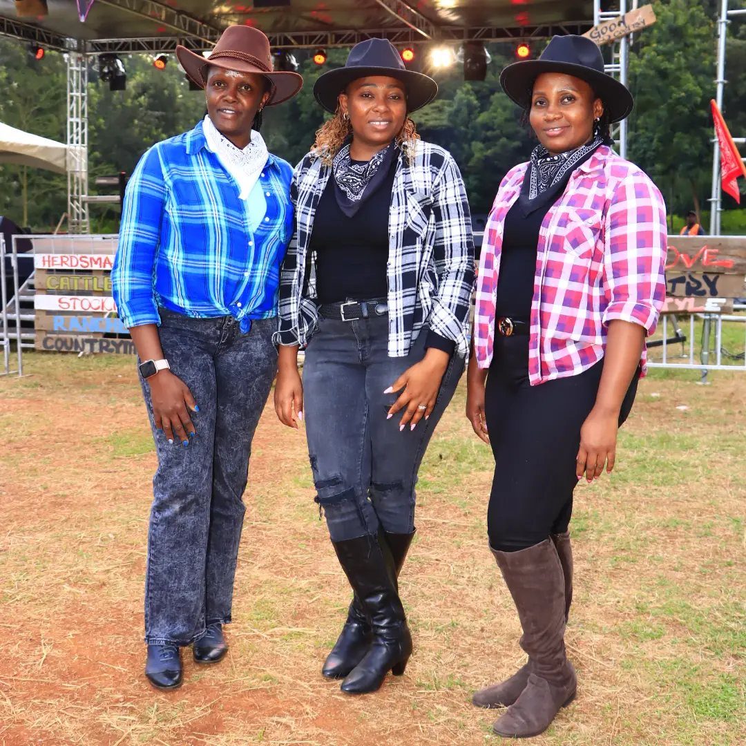 Three women in cowboy hats and plaid shirts posing at a country festival.