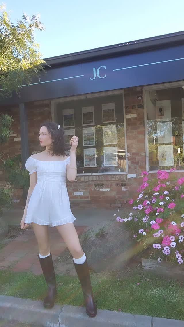 Woman wearing a short white puff-sleeve dress and tall brown leather boots outdoors.