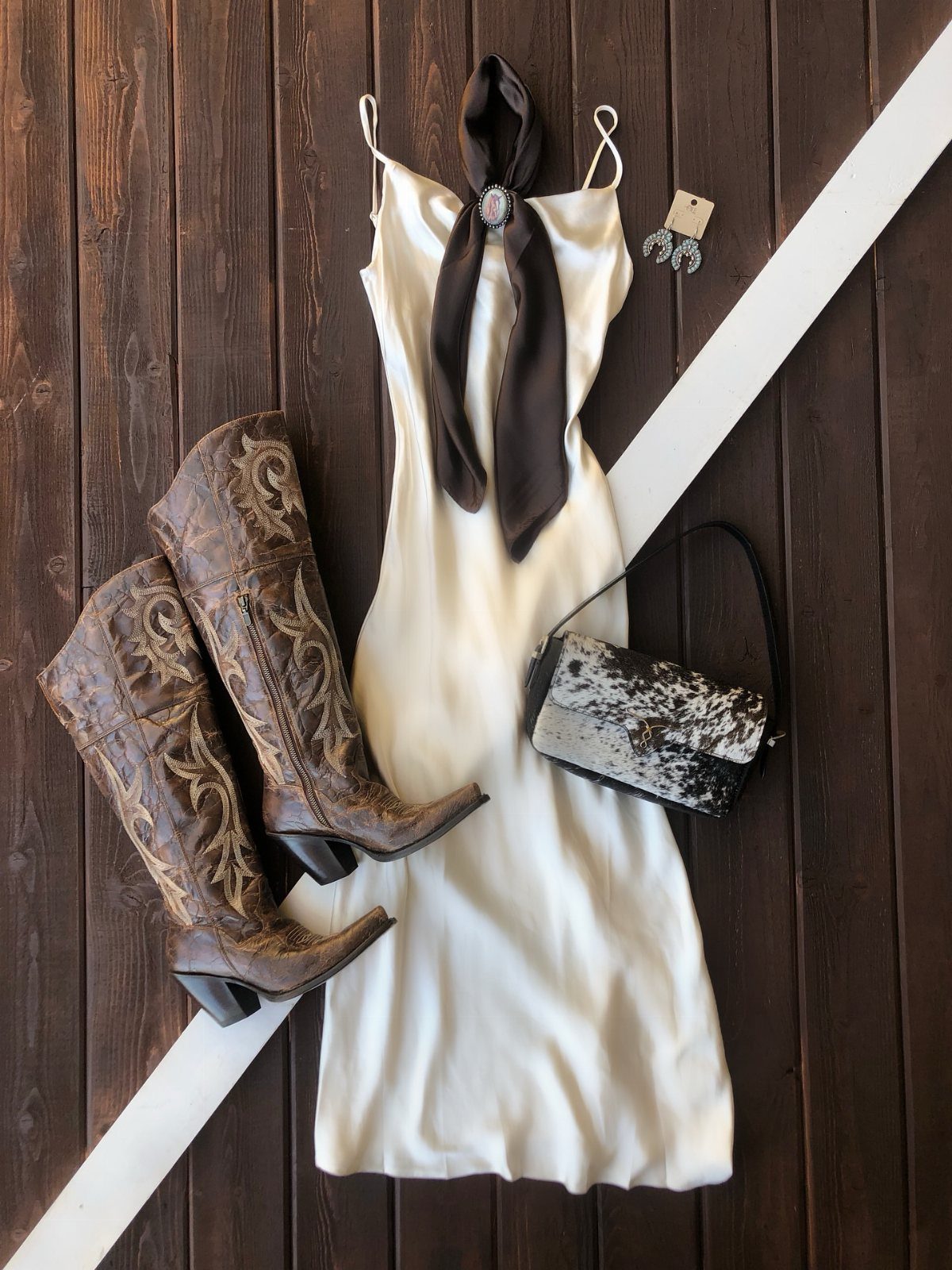 White slip dress paired with brown embroidered cowboy boots and cow-print handbag.