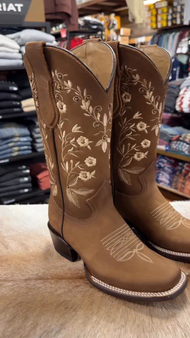 Brown leather cowboy boots with white floral embroidery on a faux fur rug.