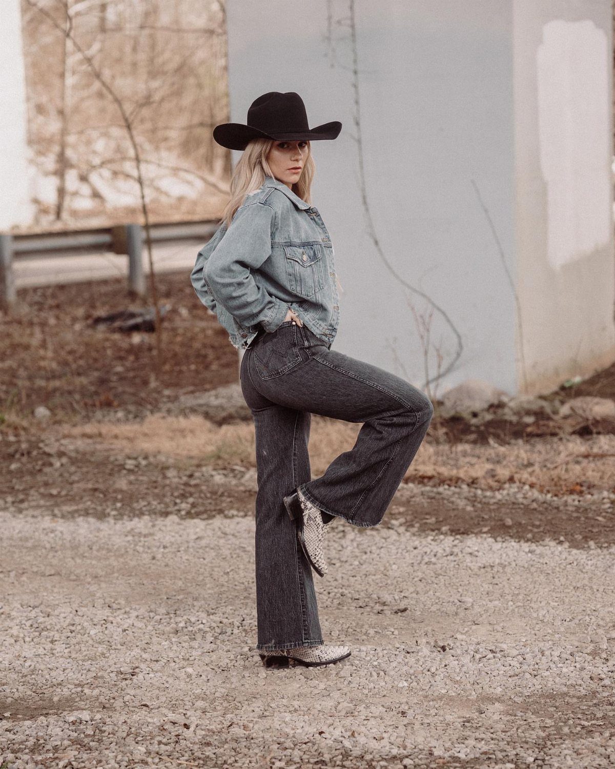 Woman in black cowboy hat and flared dark denim jeans posing outdoors.
