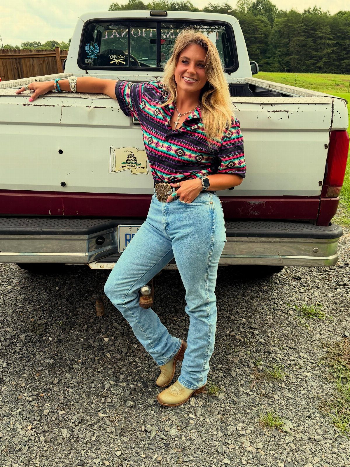 Woman in Western shirt, jeans, and cowboy boots leaning on a vintage truck.