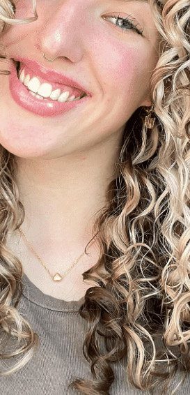 Woman with curly brunette hair and bright blonde face-framing highlights smiling for a portrait