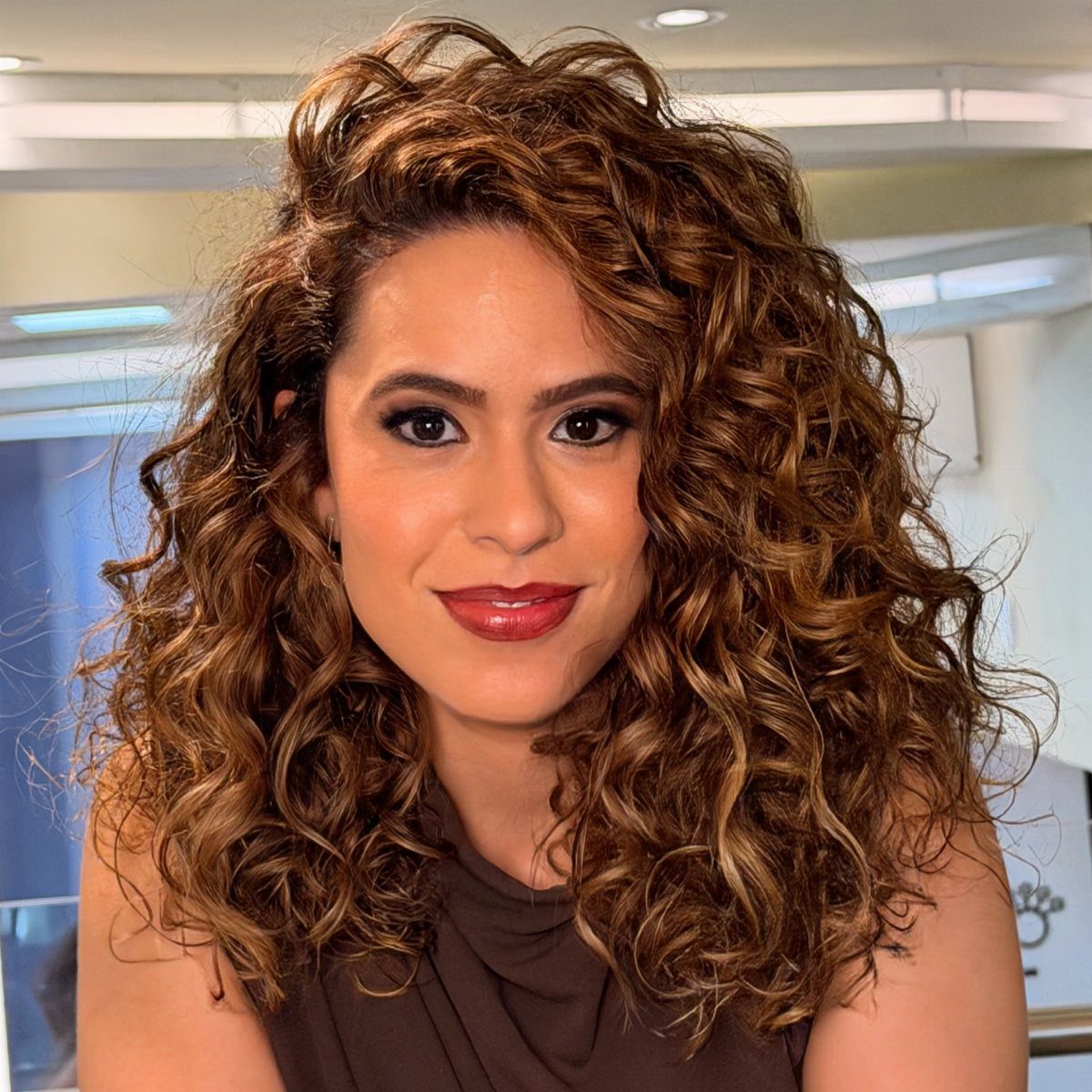 Woman with curly brunette hair and golden-blonde highlights posing for a portrait.