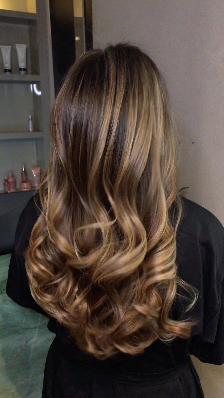 Long curly brunette hair with honey-blonde highlights styled in voluminous waves.