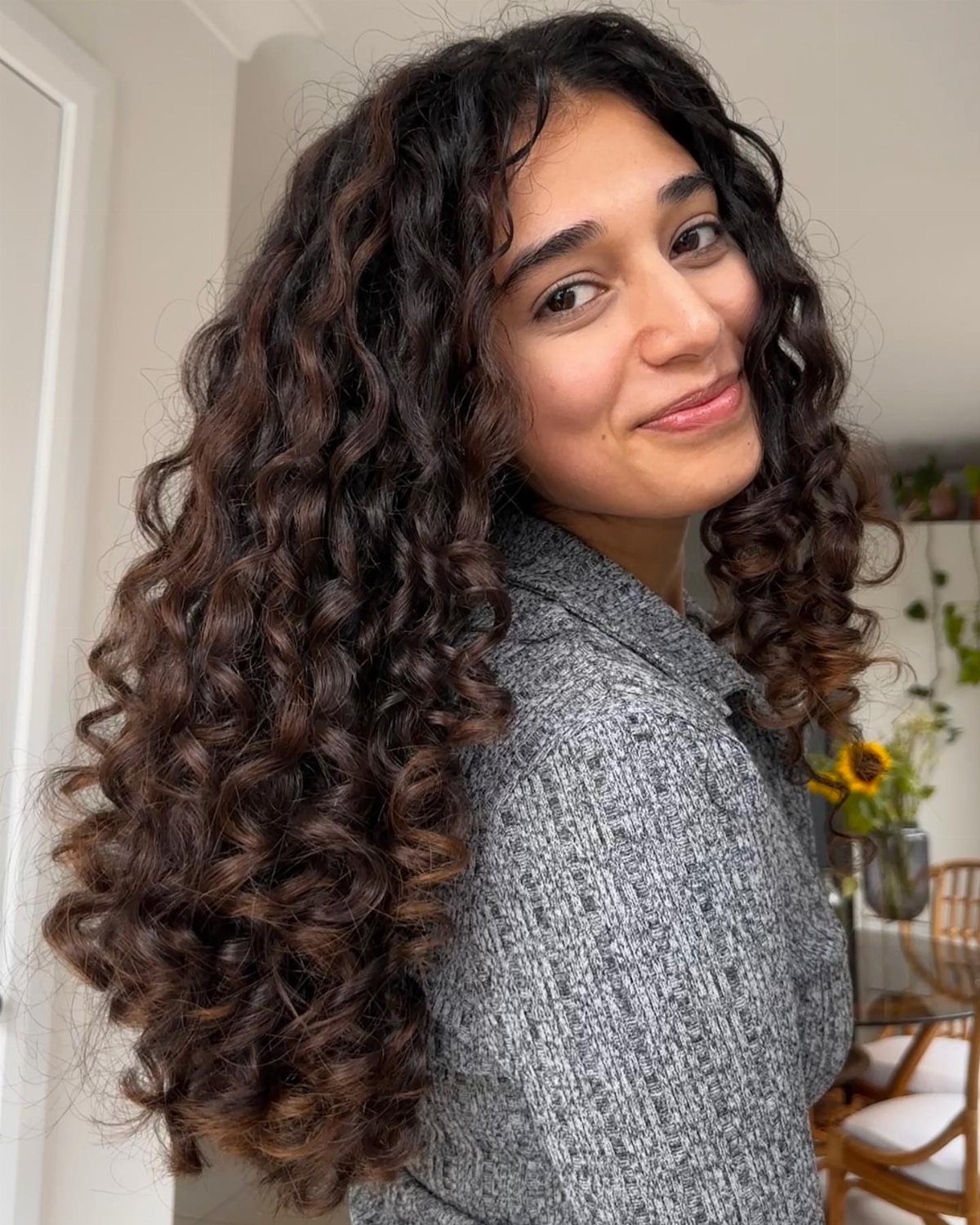 Woman with long layered curly dark brown hair and subtle warm highlights.