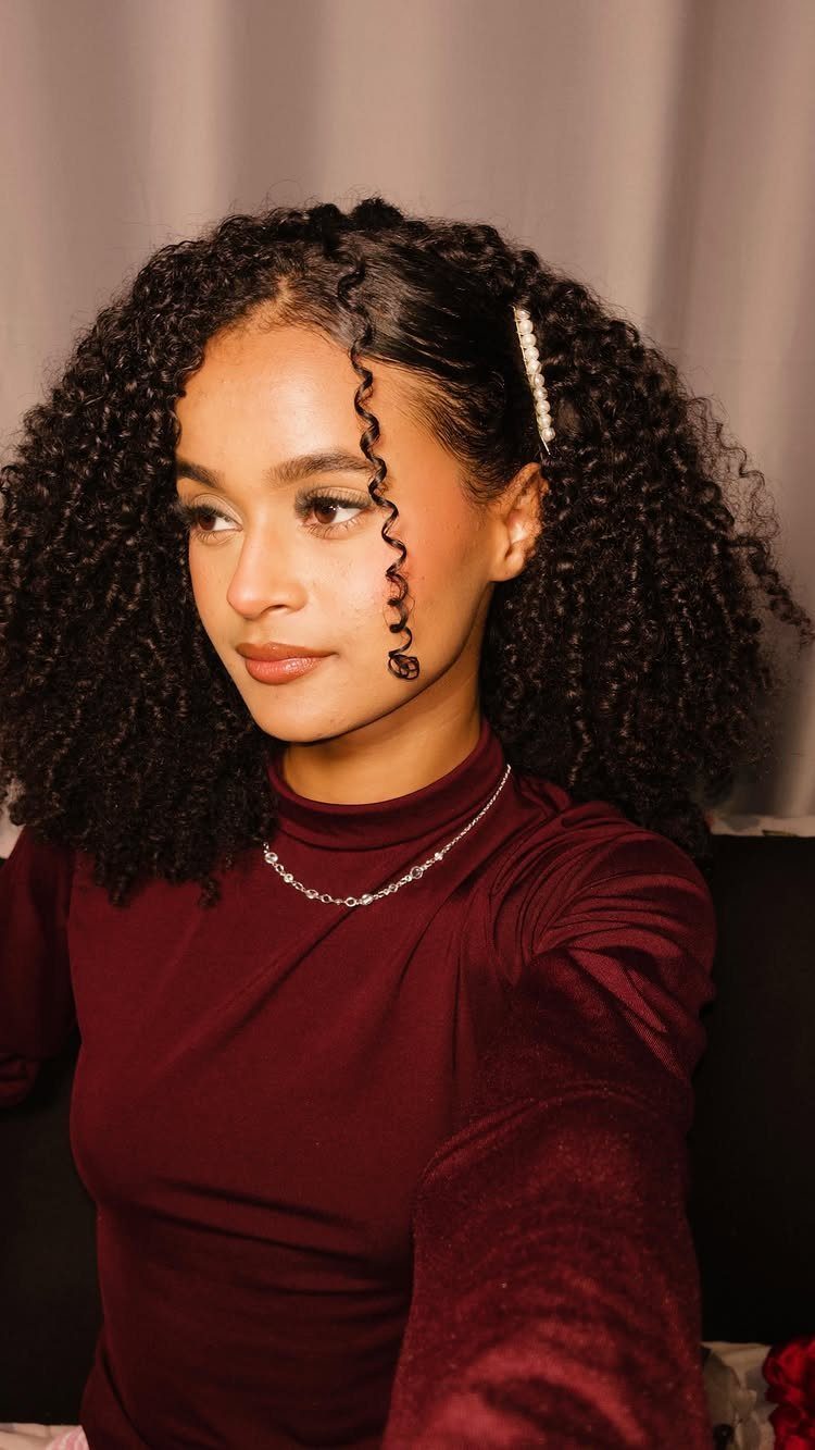 13 Curly Hair Half Up Styles with Braids, Twists and Puffs 13 Woman with curly hair in a half-up style secured with a pearl clip.
