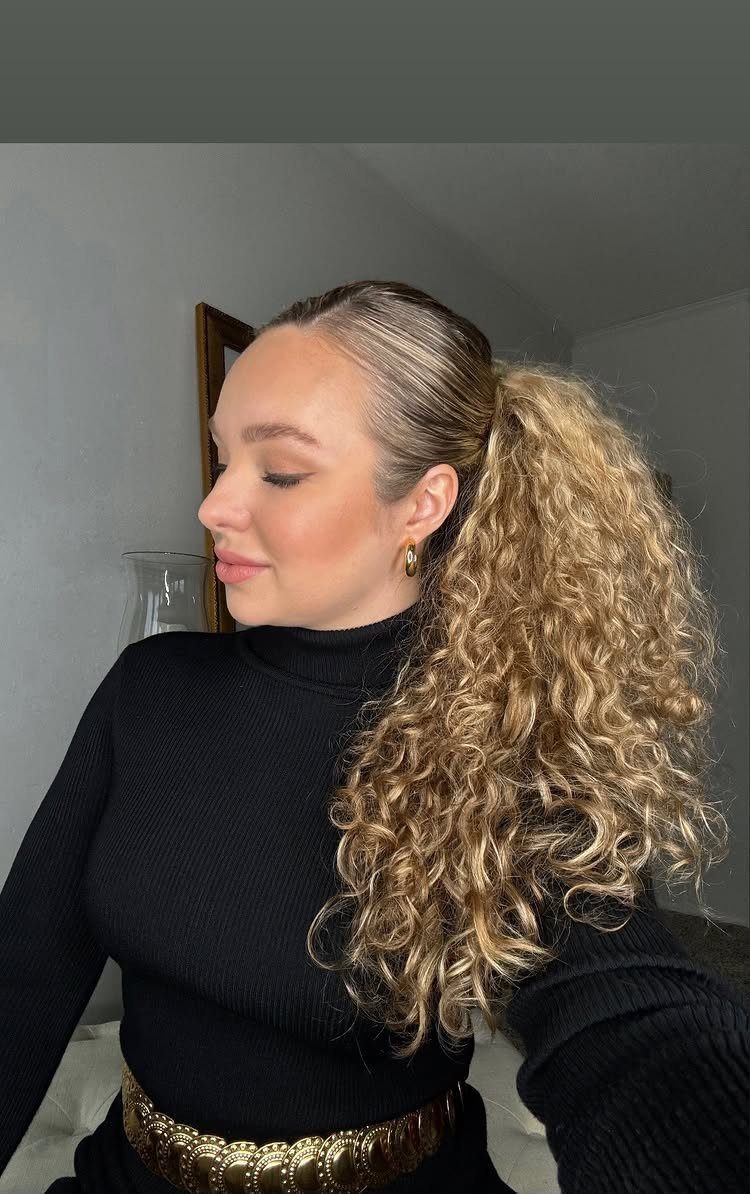 13 Curly Hair Half Up Styles with Braids, Twists and Puffs 2 Woman with blonde curly hair in a sleek half-up ponytail and black turtleneck.