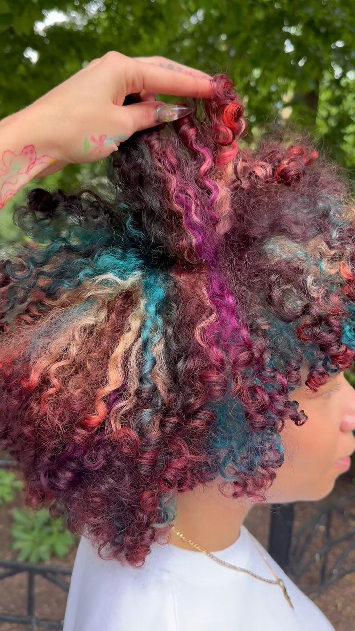 Person with voluminous curly hair dyed in magenta, teal, and blonde colors.