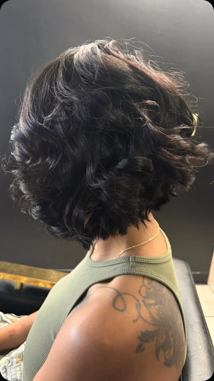 Dark curly bob haircut on a person wearing an olive green tank top.