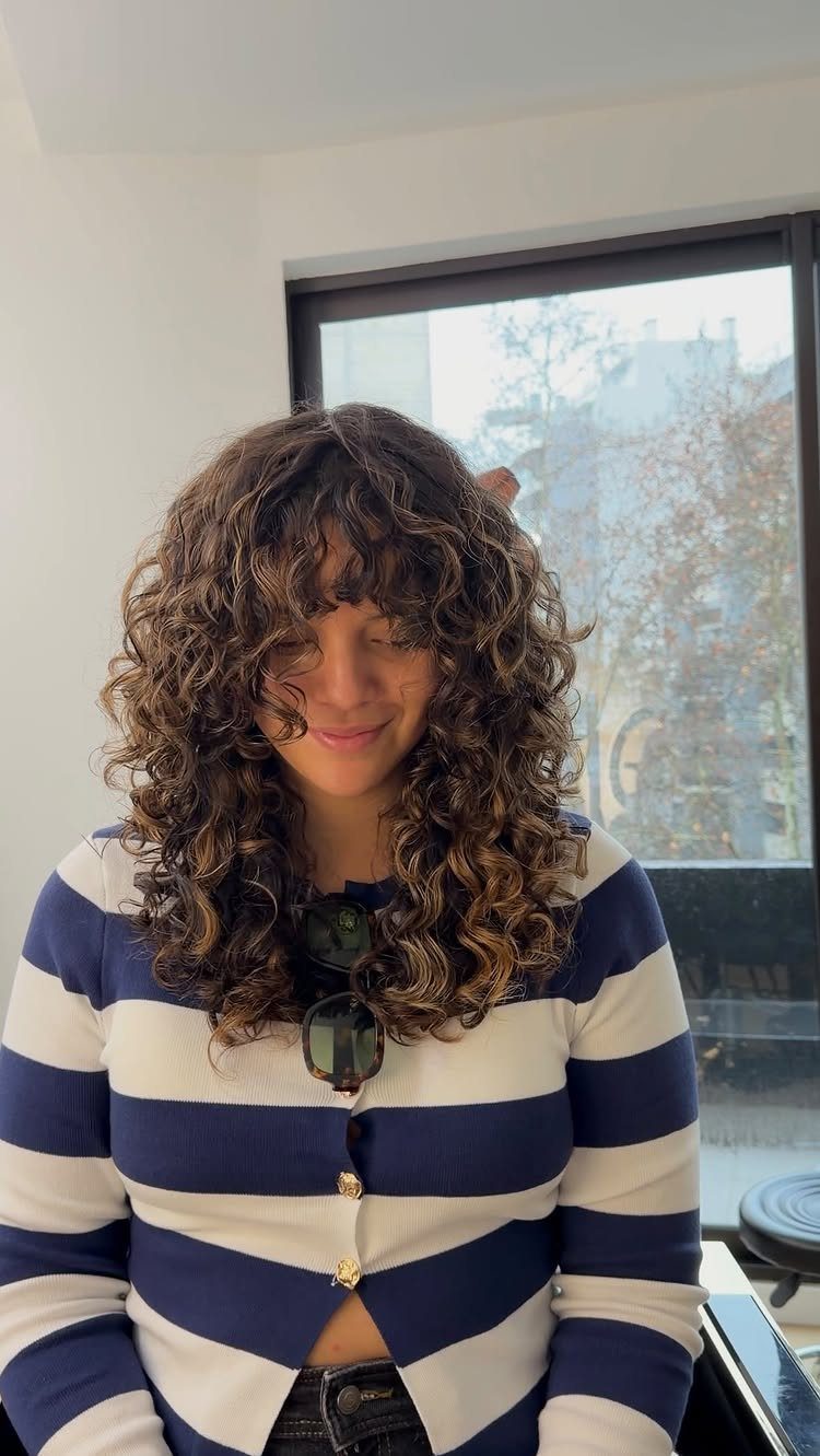 Woman with a brown curly shag haircut and bangs wearing a striped cardigan.