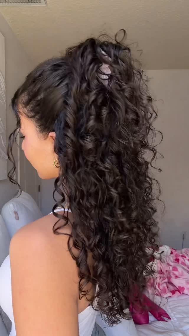 Woman with long dark curly hair styled in a half-up half-down ponytail.