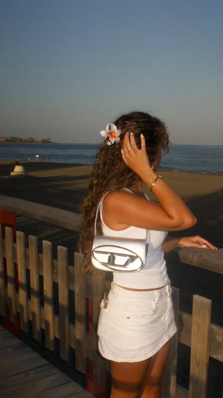 Woman with long brown curly hair and a flower on a beach boardwalk