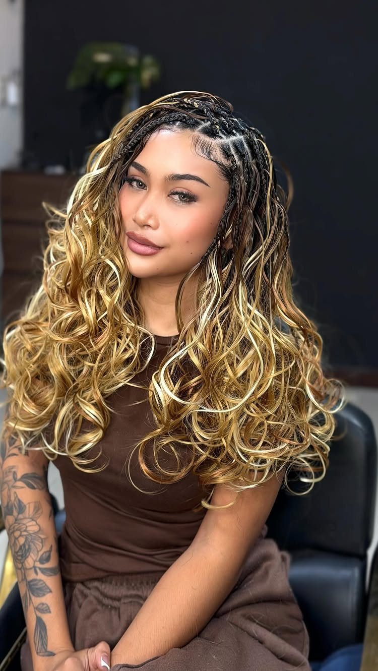 Woman with long blonde curly hair and small scalp braids wearing brown clothing.