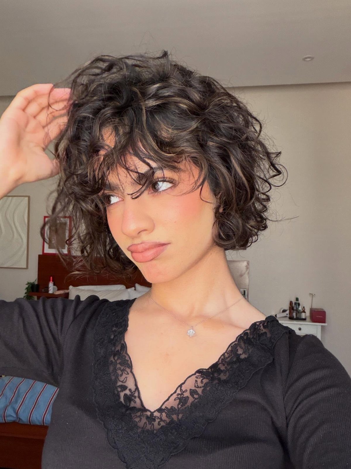 Woman with short voluminous dark curly hair and bangs wearing a black lace top.