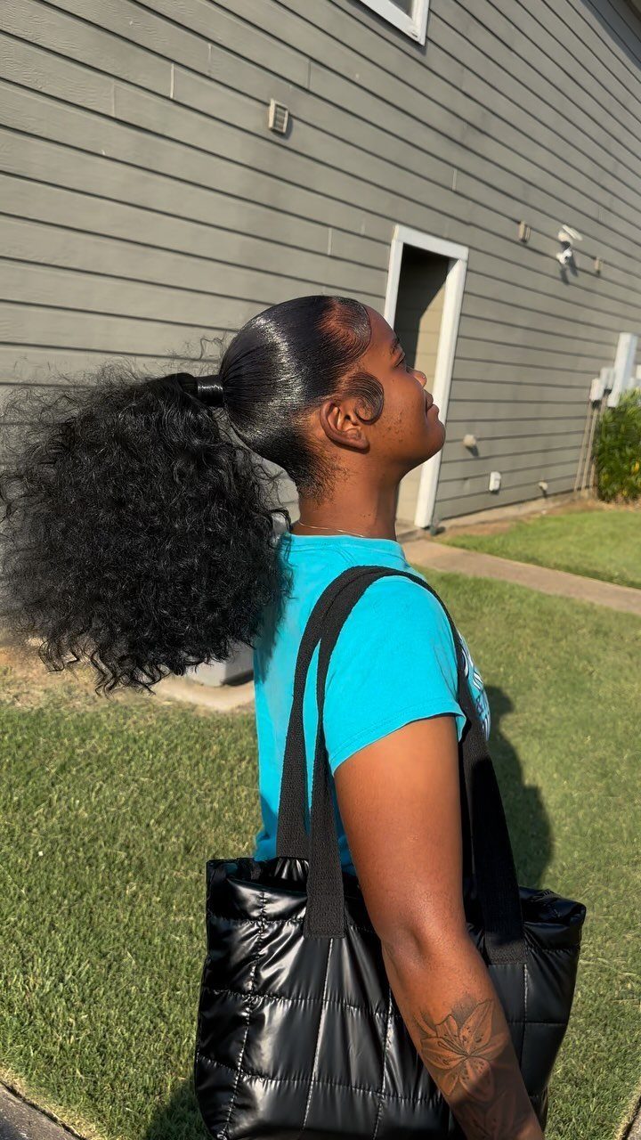 Woman with a slicked-back ponytail and voluminous curly hair wearing a blue shirt.