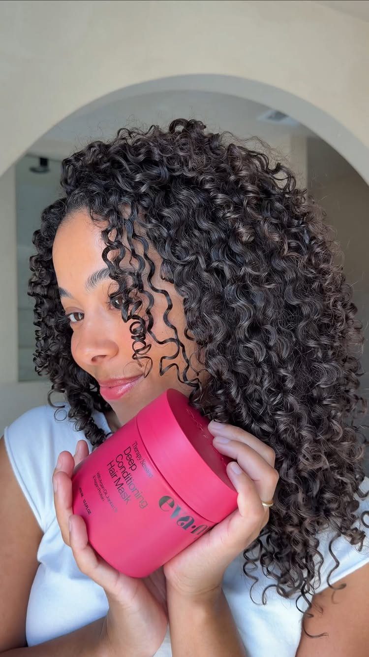 Woman with curly hair holding a pink tub of deep conditioning hair mask.