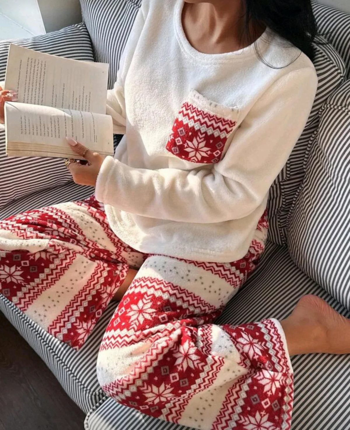 Person in white and red snowflake print pajamas reading a book on a sofa