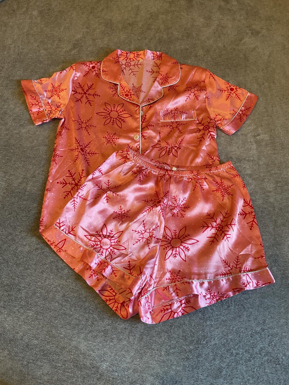 Pink satin pajama set with red snowflake prints laid on grey fabric