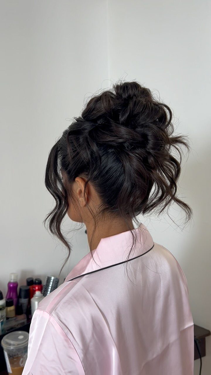 Woman with dark brown hair styled in a voluminous curly updo wearing pink satin.