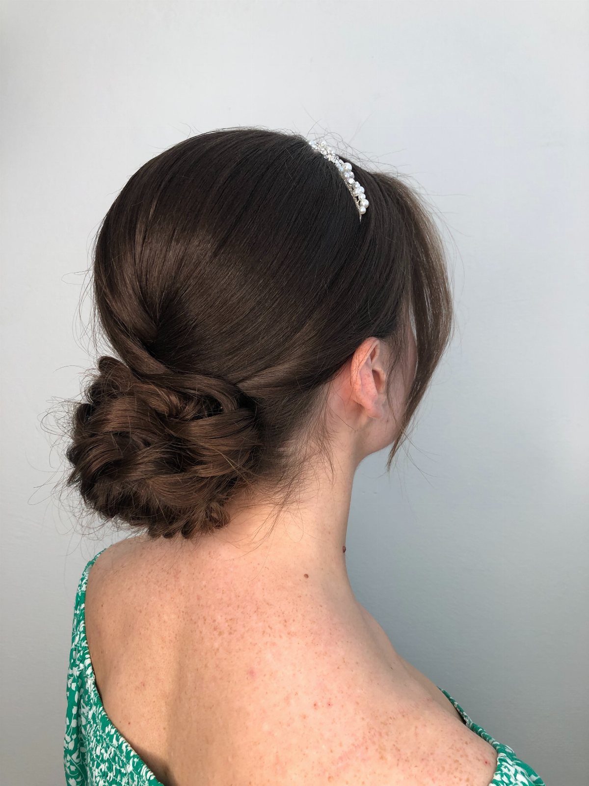 Woman with brown hair in a low bun wearing a white beaded headband.