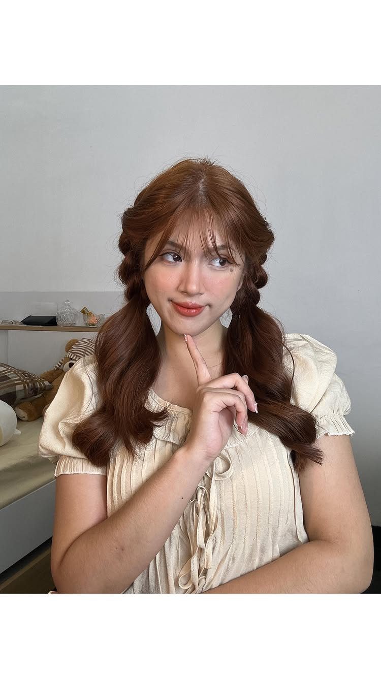 Woman with reddish-brown hair styled in low pigtails with braided crown sections.