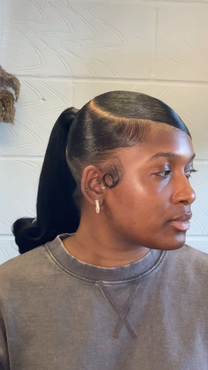 Woman with a sleek ponytail, precise side part, and styled edges against white wall.