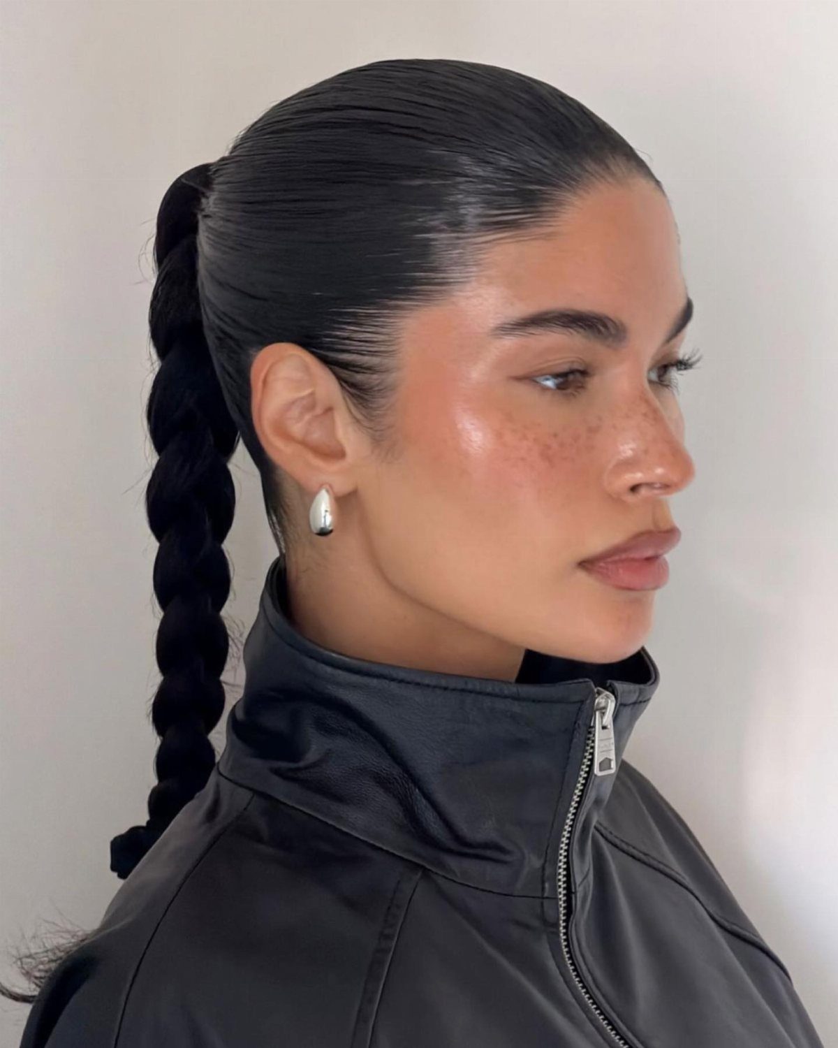 Woman with slicked back hair in a braided ponytail wearing a black leather jacket.