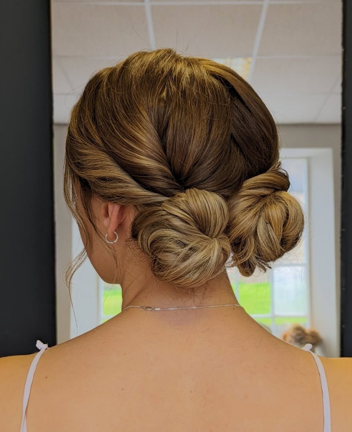 Light brown hair styled into two low space buns at the nape.