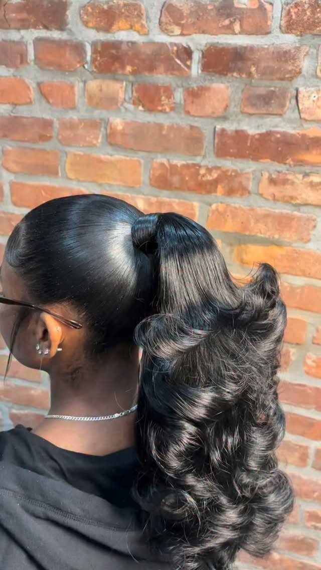 18 Cute Ponytail Hairstyles for Every Mood and Length 11 Sleek high ponytail with voluminous curls against a red brick wall background.