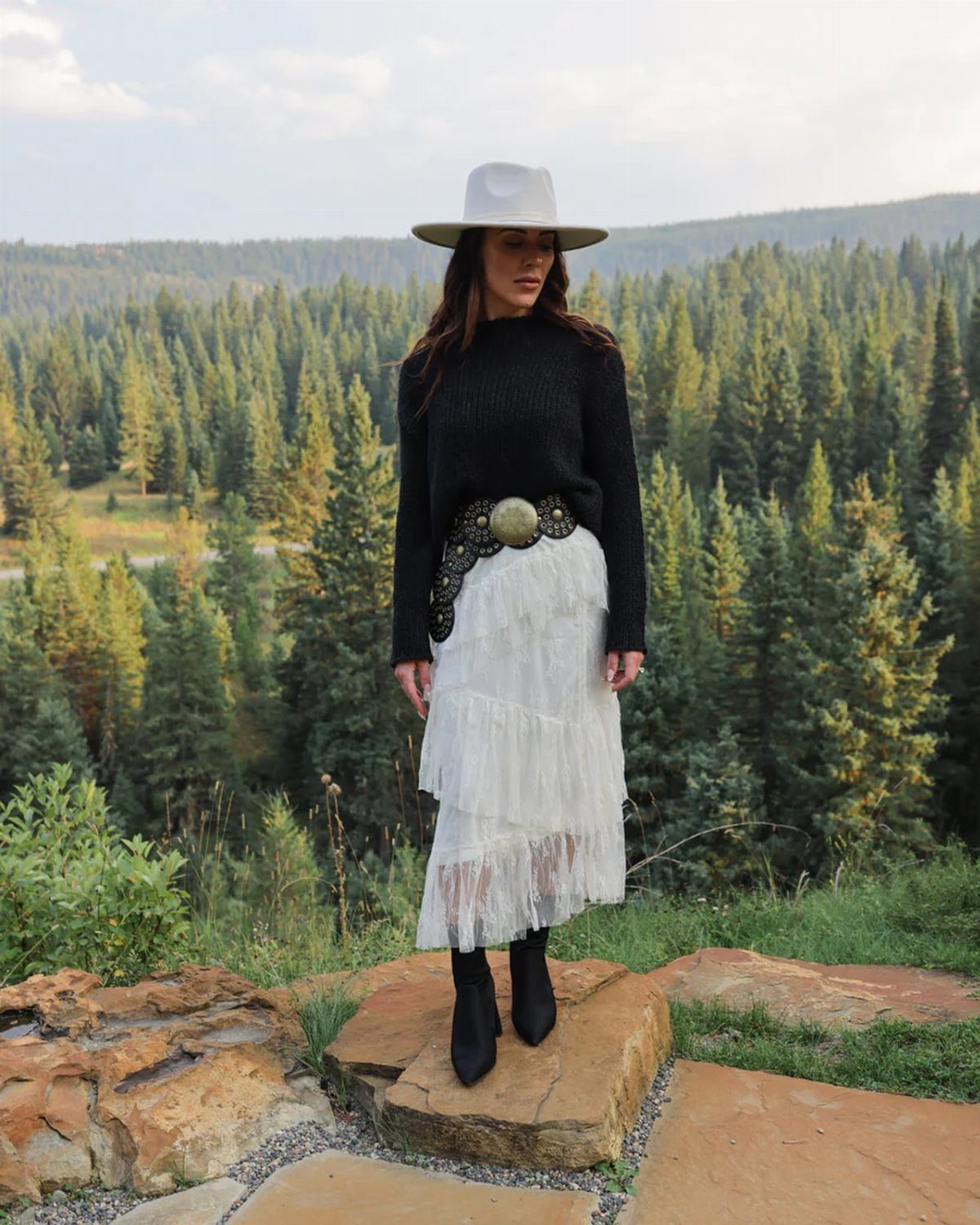 Cute Western Outfits for Women: 13 Ideas to Wear Now 10 Woman in black sweater and white tiered lace skirt posing in a forest