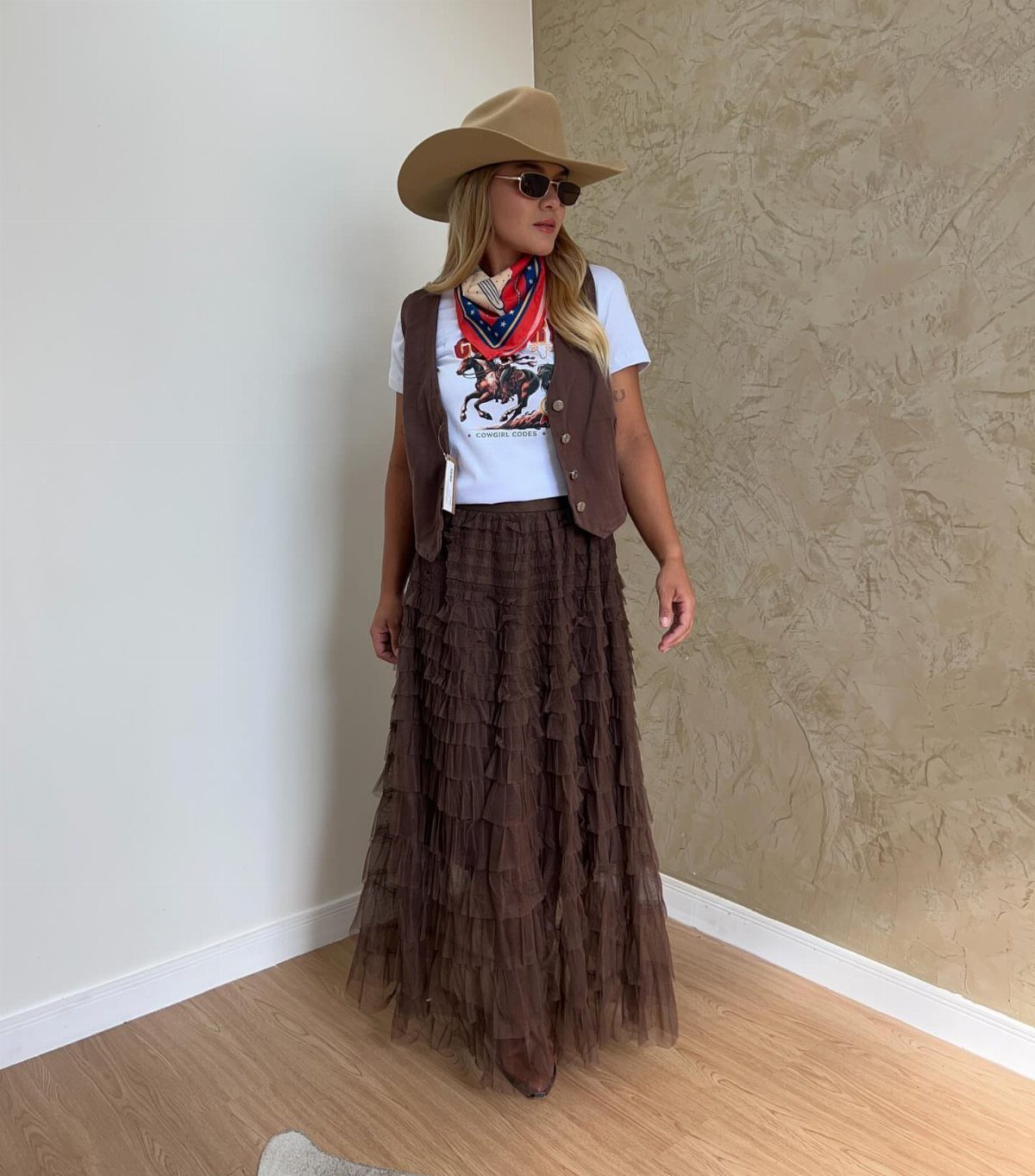 Cute Western Outfits for Women: 13 Ideas to Wear Now 9 Woman in cowboy hat, brown vest, and tiered brown ruffled maxi skirt indoors.