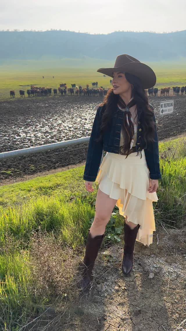 Cute Western Outfits for Women: 13 Ideas to Wear Now 5 Woman in a ruffled cream dress, blue jacket, and brown cowgirl boots outdoors.