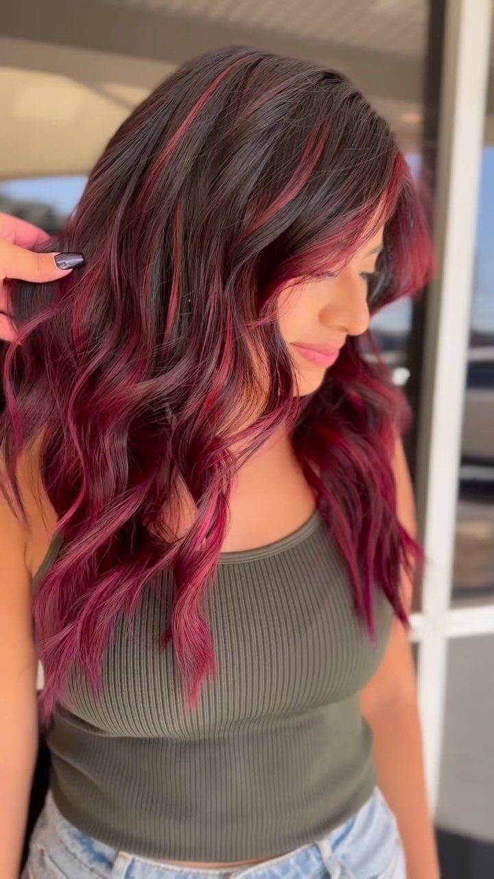 5 Dark Crimson Hair Ideas, From Merlot to Copper Tones 2 Woman with long wavy dark hair and vibrant ruby red highlights wearing green top