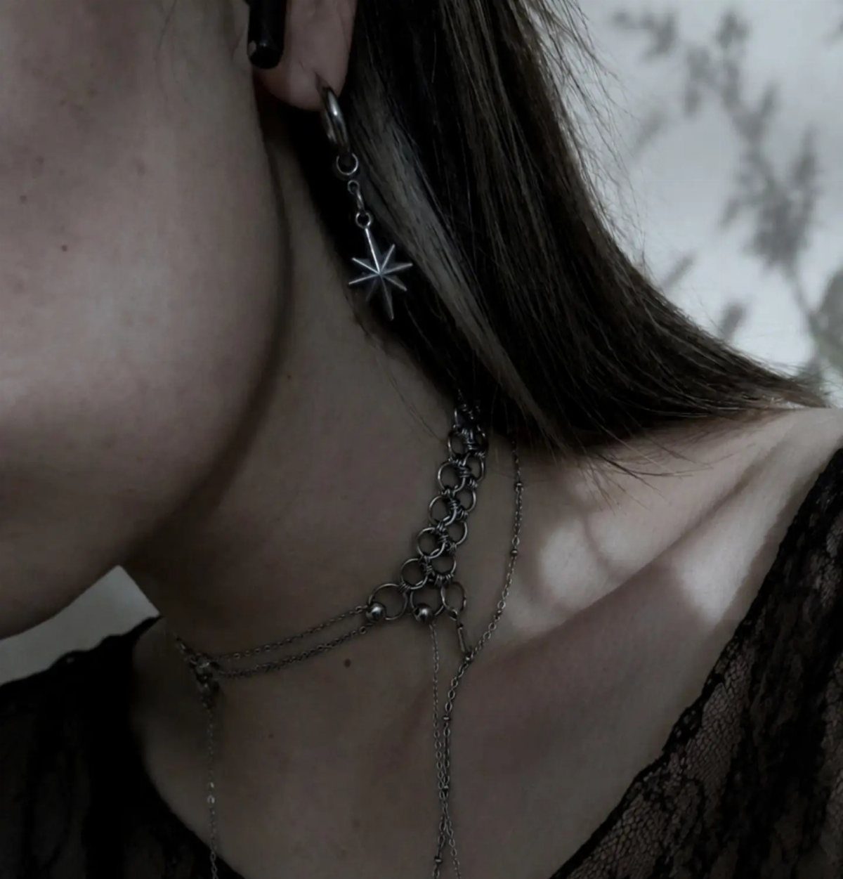 Silver star earring and chunky chain necklace worn with black lace clothing.