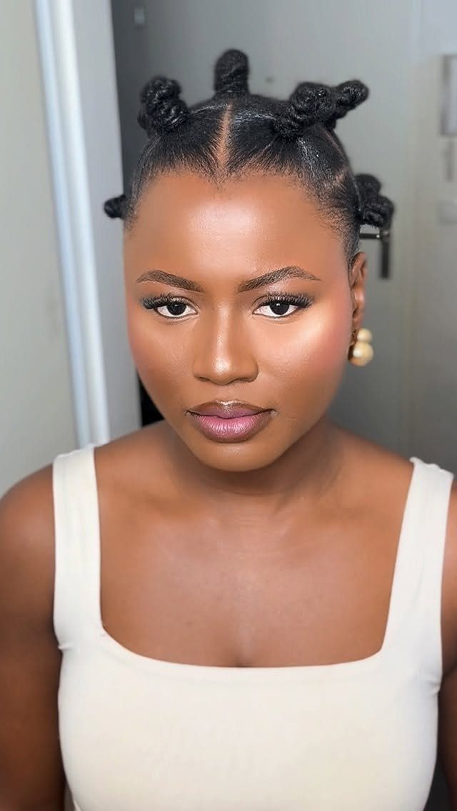 Woman with dark skin wearing Bantu knots hairstyle and a white top.