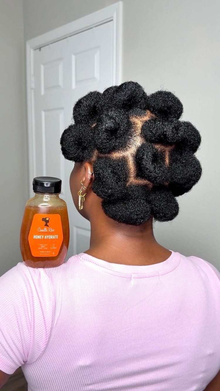 Person with defined 4c hair styled in coiled buns and a hair product bottle.