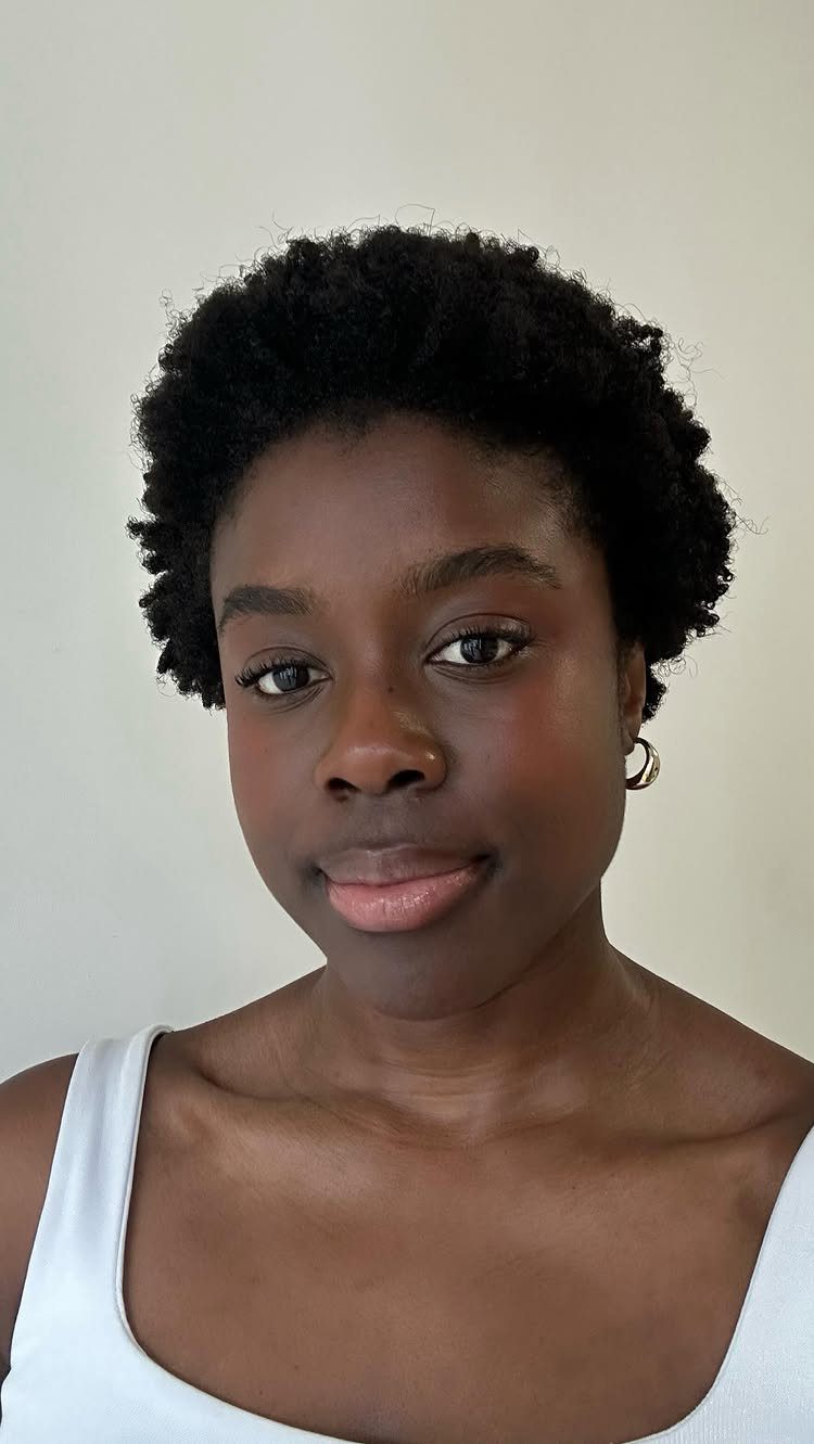 Black woman with short, natural 4C hair wearing a white tank top.