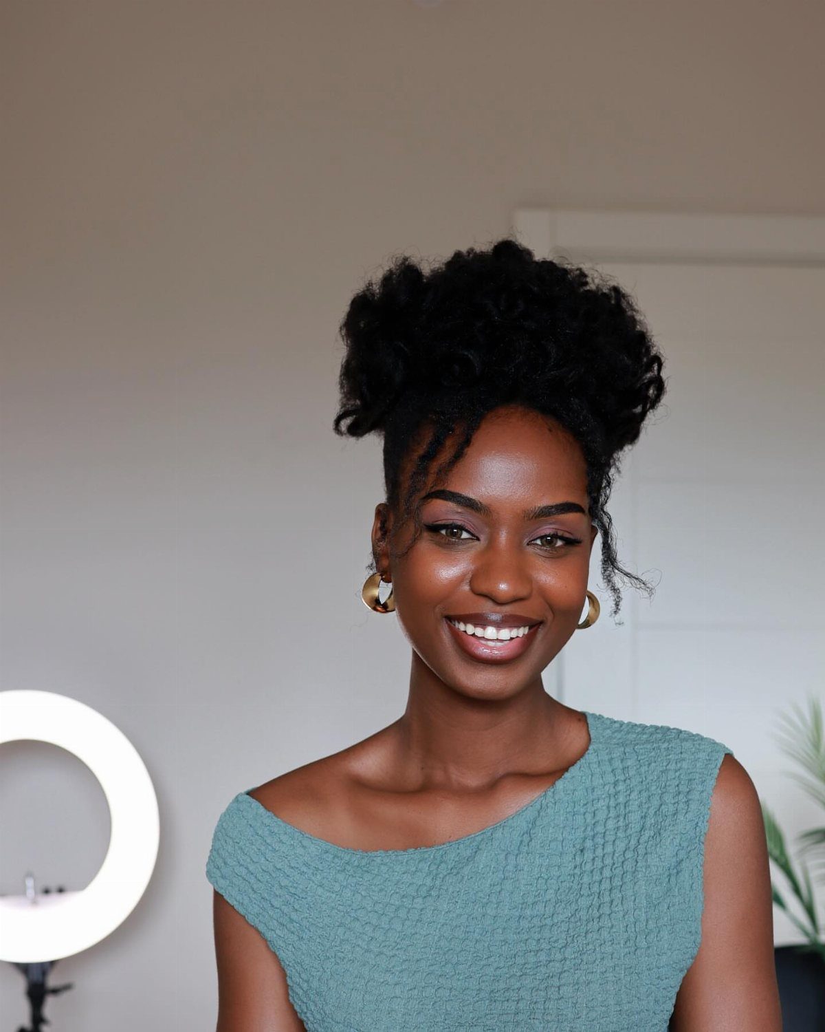 Black woman with defined 4c curly hair styled in a high updo smiling