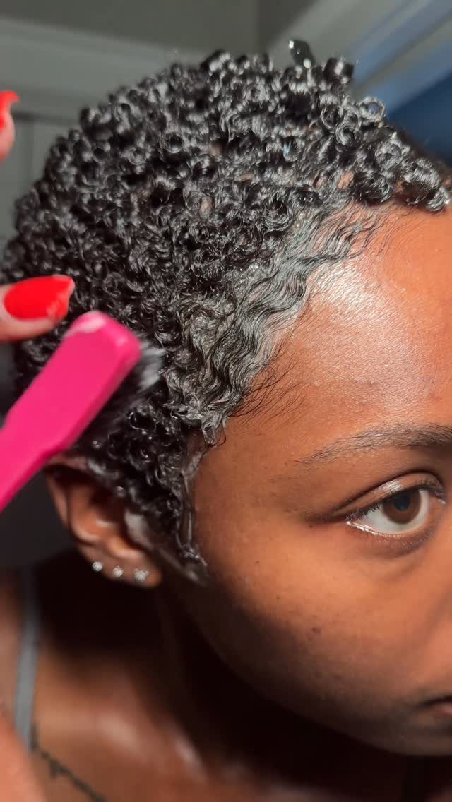 Tightly coiled 4C hair being styled with a pink comb near the temple.