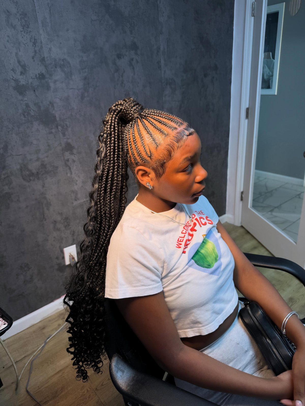 Young woman with cornrows styled into a long, high braided ponytail with curly ends.