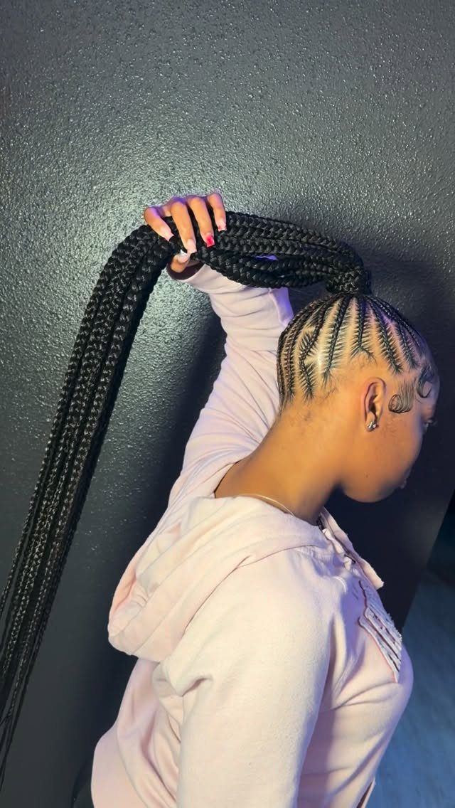 Woman with cornrows transitioning into a long black braided ponytail wearing a pink hoodie.