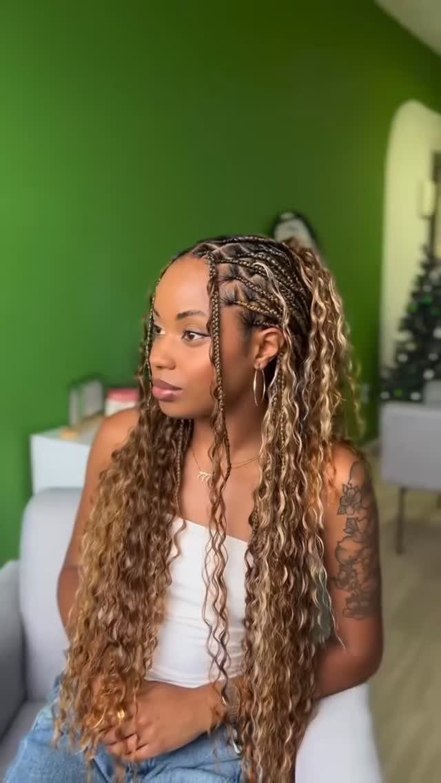 Woman with long blonde goddess braids with curly ends against a green wall