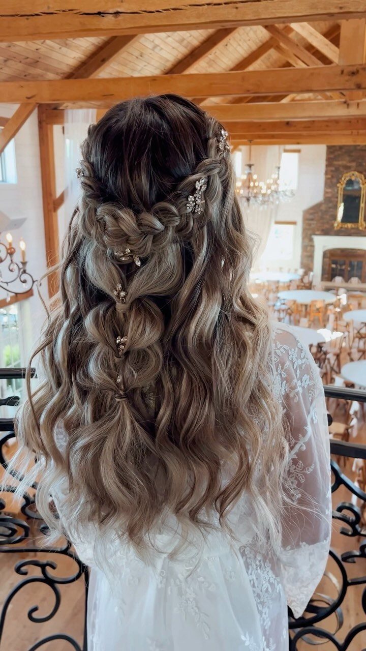 Woman with long wavy brown hair in a braided half-updo with decorative pins.