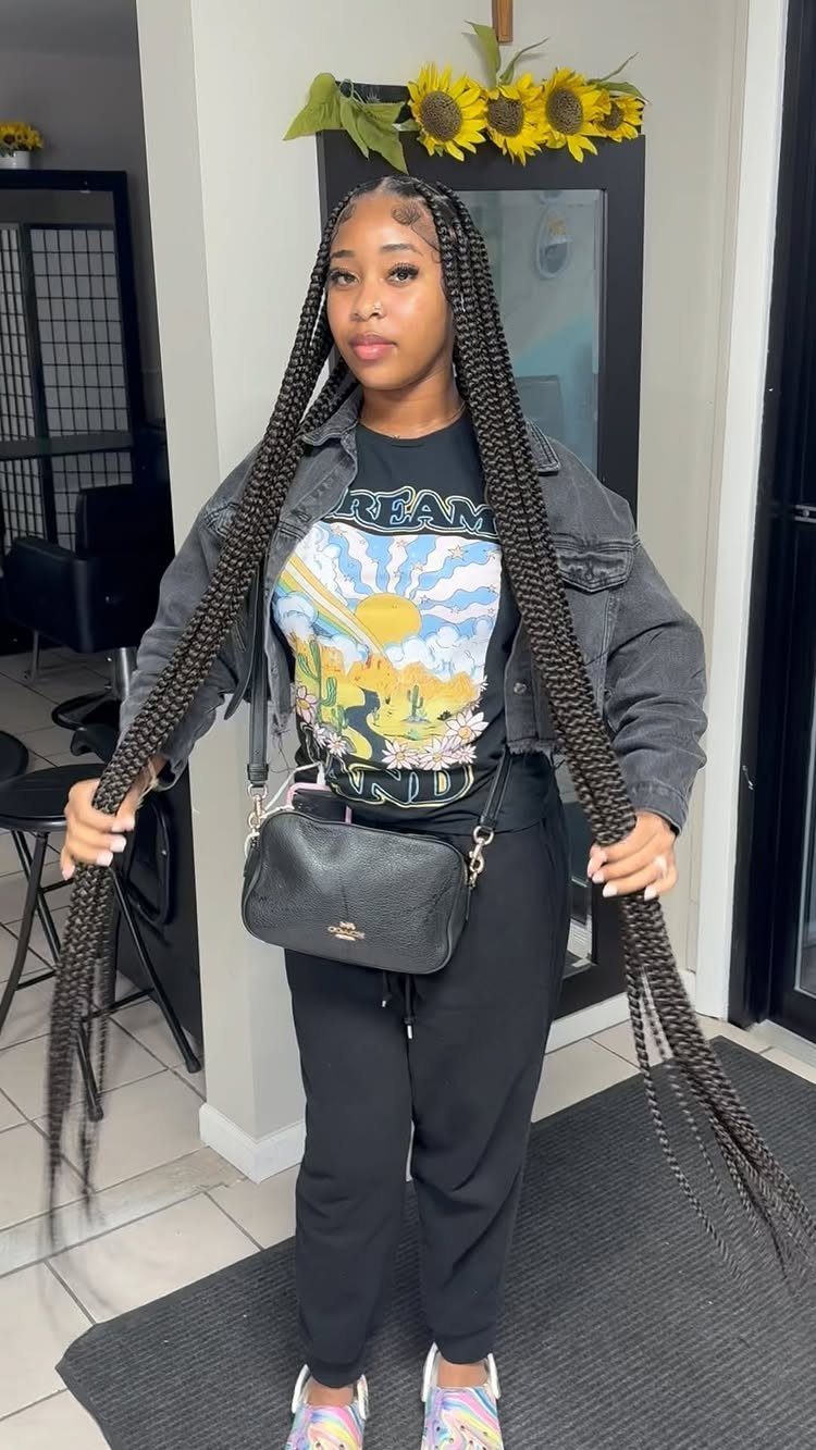 Woman with long, thick black jumbo braids wearing a grey denim jacket and t-shirt.