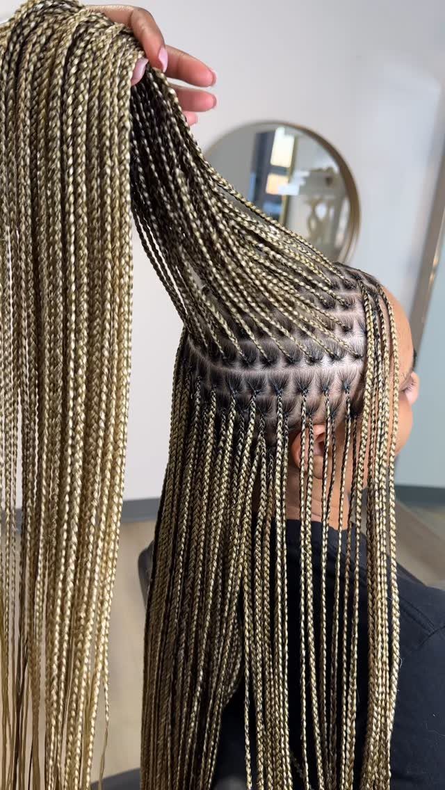 Long blonde and brown knotless braids held up to show the scalp parting.